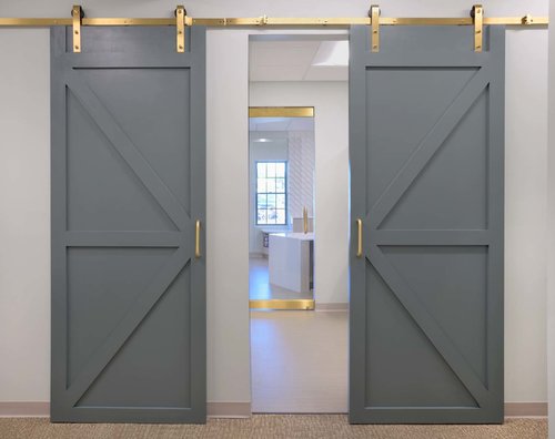 Signature gray barn doors with brass hardware leading into the clinical area at Monroe Eye Care